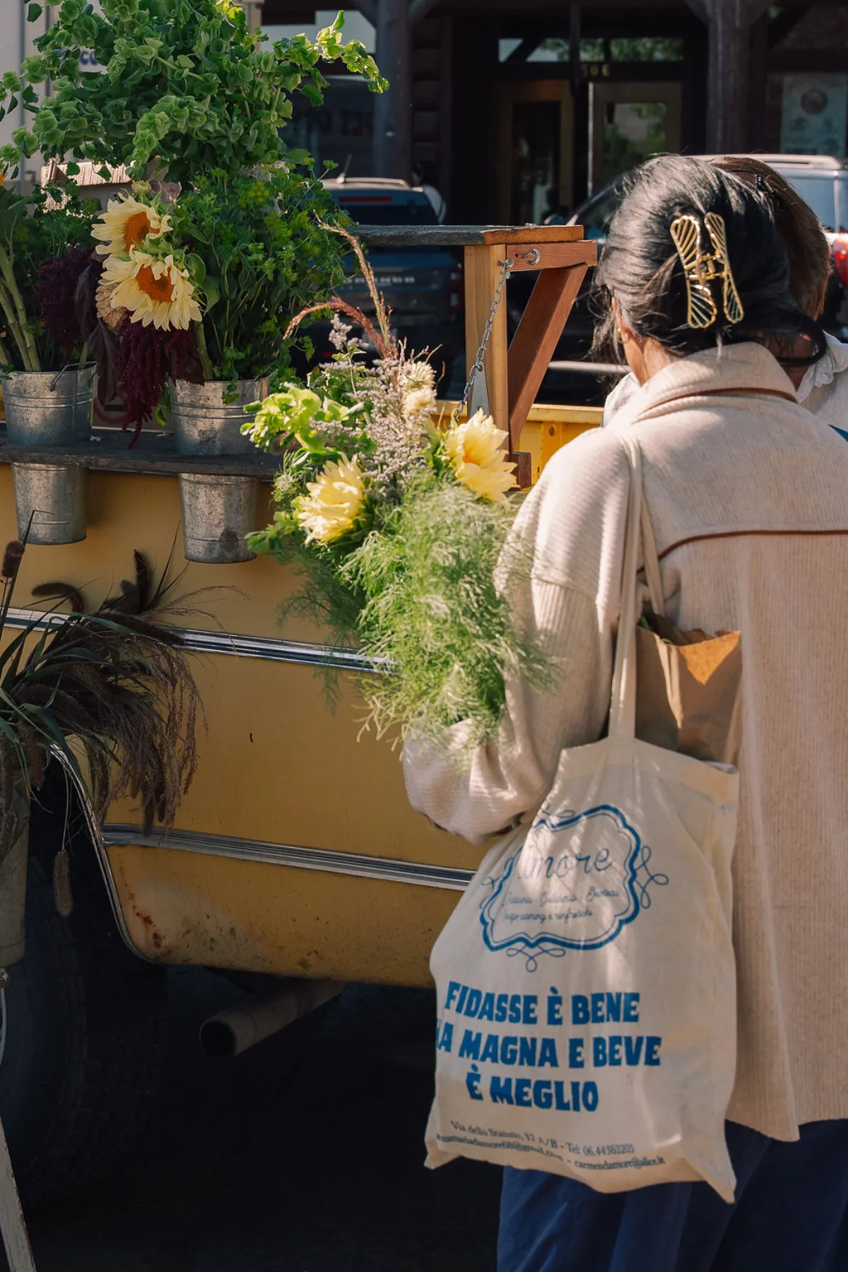 Shopper browsing fresh flowers at a vintage yellow truck vendor